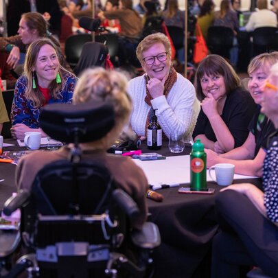 A group of people of varying abilities seated around a table at a conference.