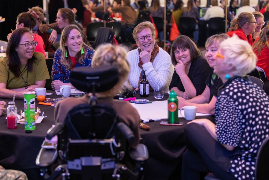 A group of people of varying abilities seated around a table at a conference.