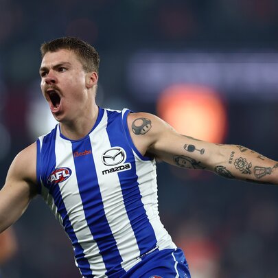 A North Melbourne AFL football player running with arms outstretched as if cheering himself and his teams on during a match.