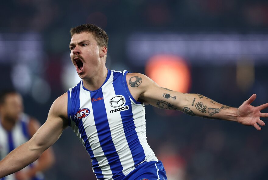 A North Melbourne AFL football player running with arms outstretched as if cheering himself and his teams on during a match.