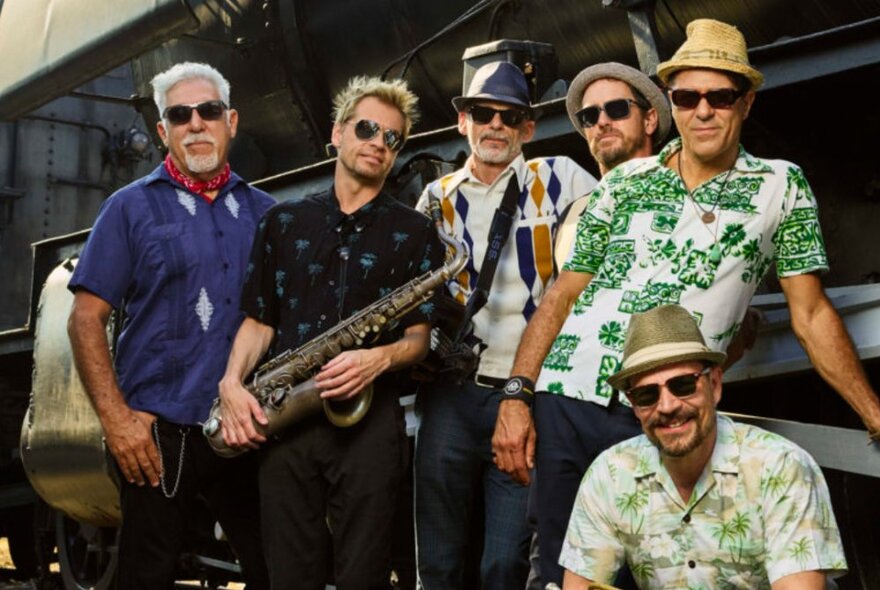 White calypso reggae band wearing hats, shades and loud shirts, one musician holding a saxophone.