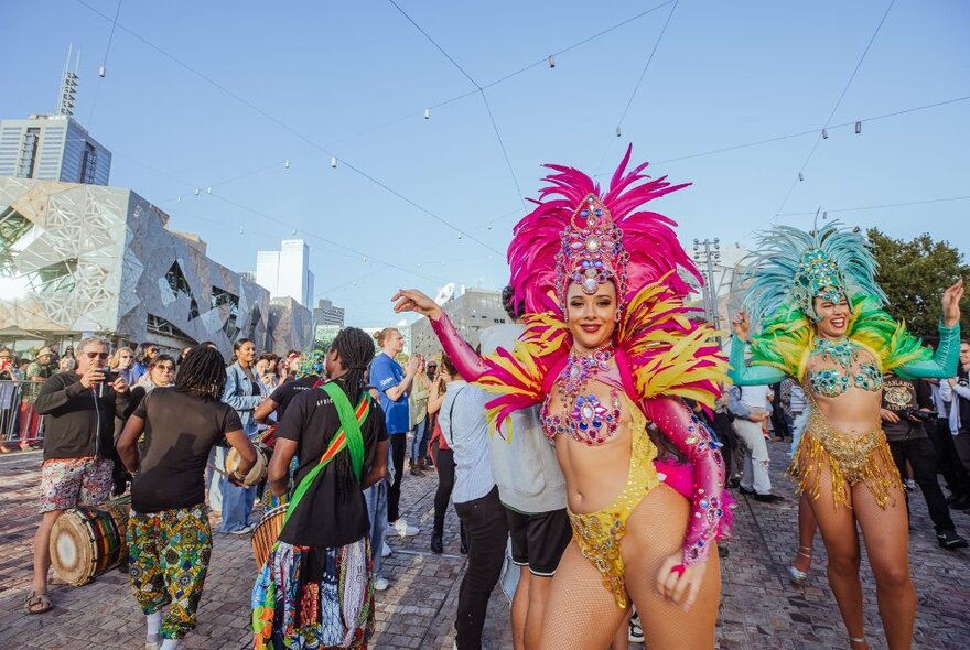 Dancers in elaborate Carnival style costumes walking through the crowds at a daytime festival at Fed Square.