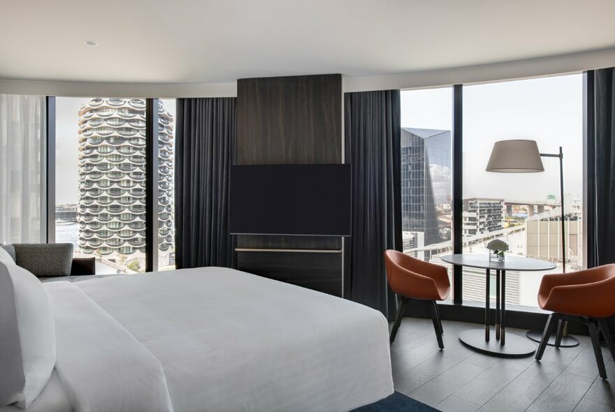 A deluxe room at the Melbourne Marriott Hotel, with wide windows and a queen size bed in the foreground with white sheets.