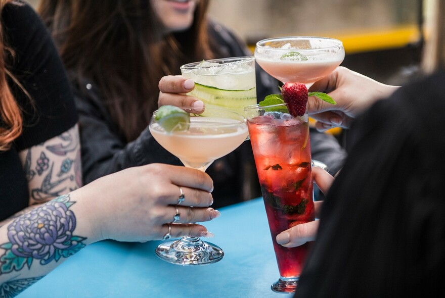 Four sets of hands clinking their cocktail glasses together in a 'cheers' gesture.