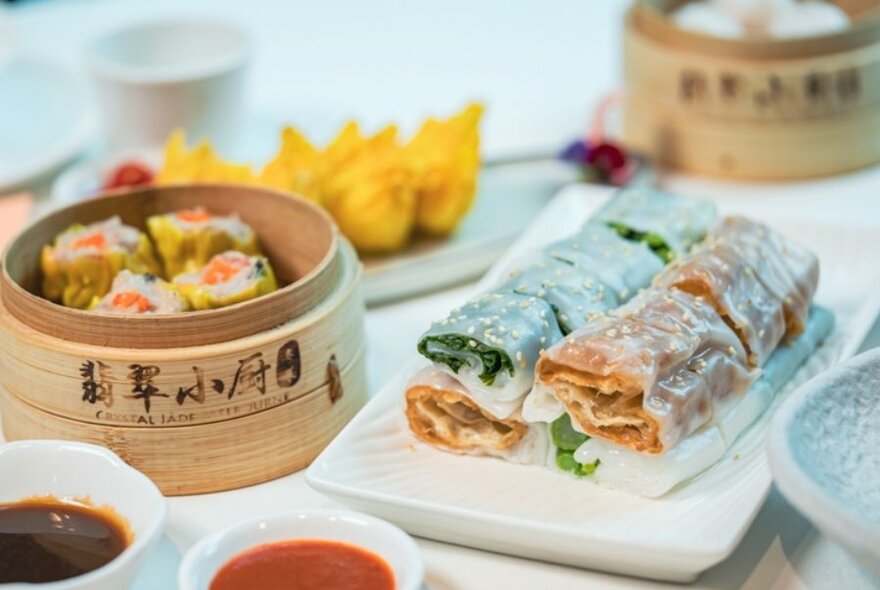 Asian dishes on a table, including steamer with dumplings, condiments and wraps.