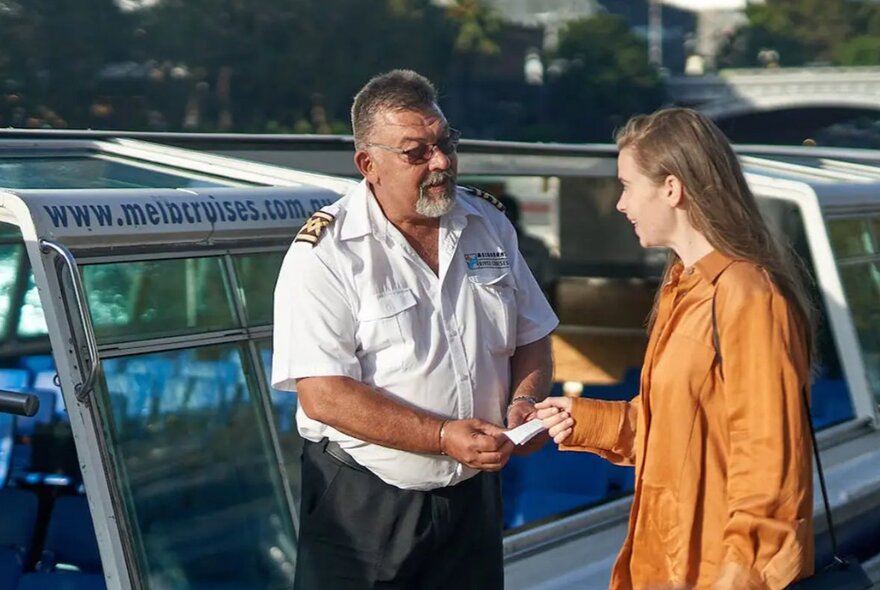A captain in a white shirt welcoming a passenger on to a cruise boat.