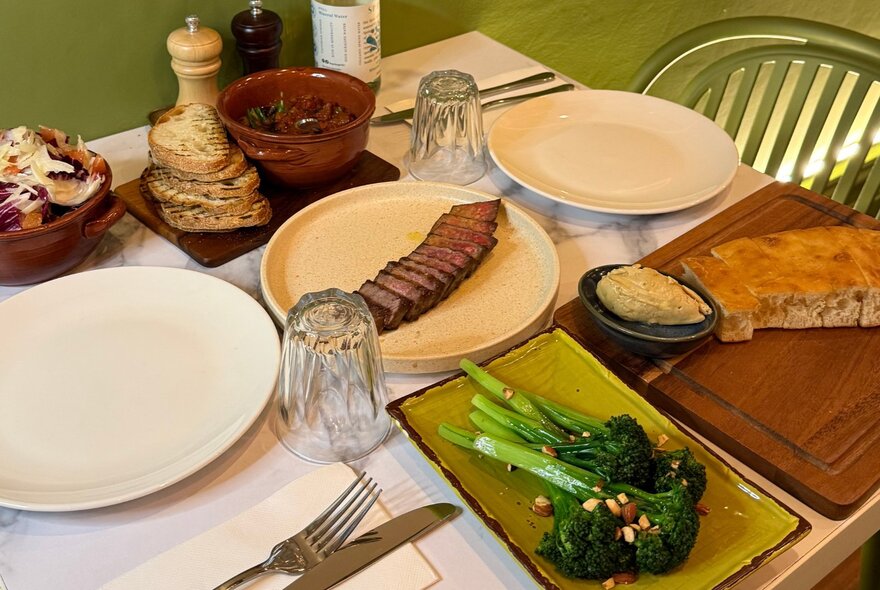 A restaurant dining table that includes a sliced steak, focaccia, and broccolini.