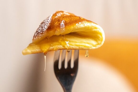 A doubled-over slice of honey soaked pancake being held up on a fork.