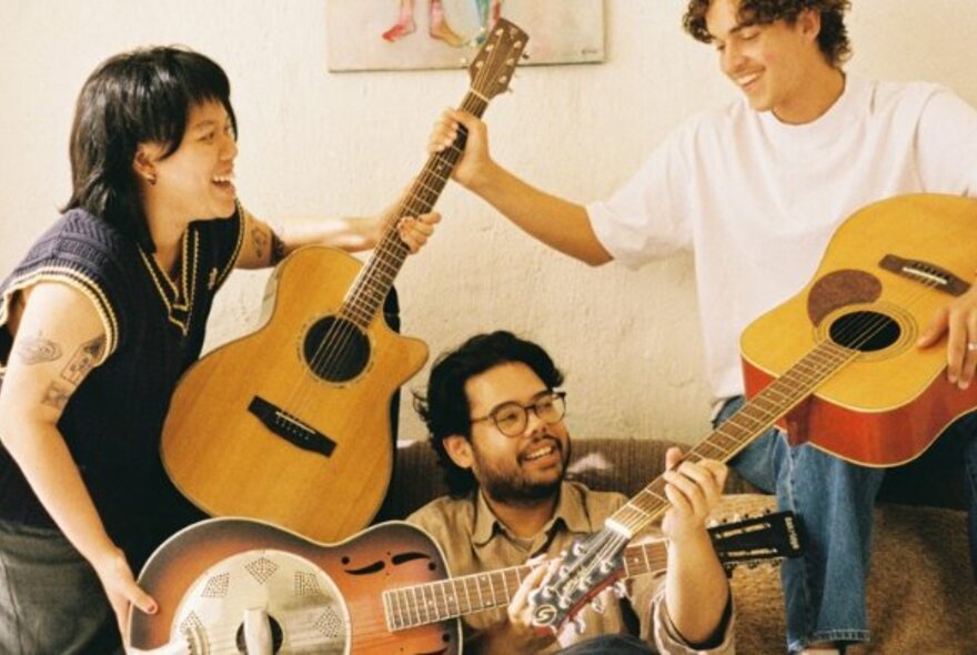 Three queer folk artists laughing and jamming together with their guitars.