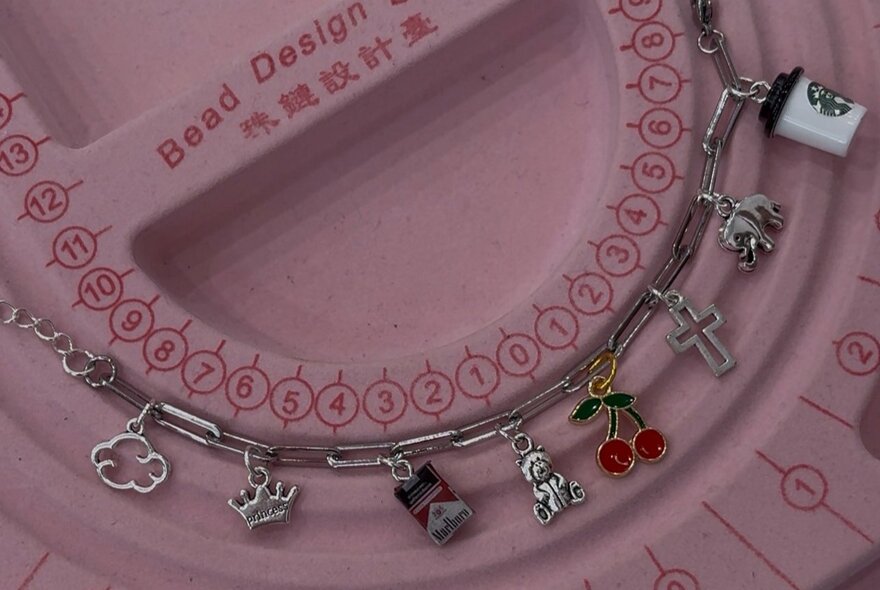 A silver bracelet with many small charms on a pink design template. 