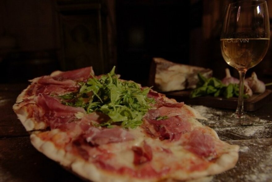 Pizza with sliced meat and basil leaf topping.