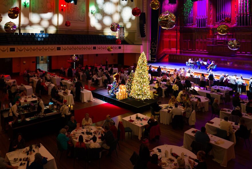 The inside of Melbourne's Town Hall, set with tables and chairs plus a glowing Christmas tree for a Christmas buffet.