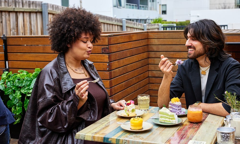 Two friends sharing colourful drinks and cakes at an outdoor cafe.