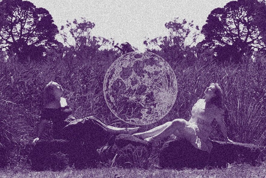 Purple-hued image of two women lying on the grass next to a huge orb.