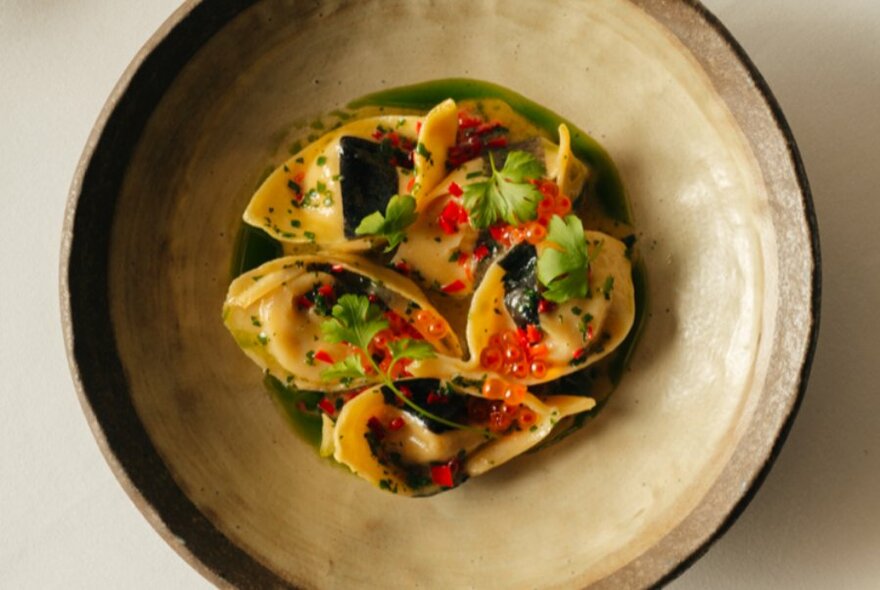 Cream clay bowl of filled pasta, garnished with parsley and roe.