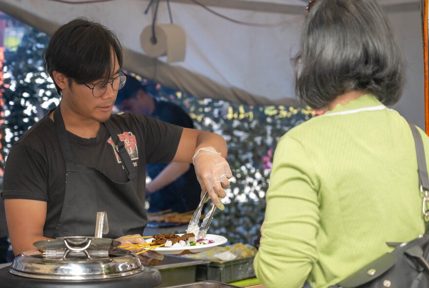 A man serving a woman a plate of Indonesian food at a food stall.