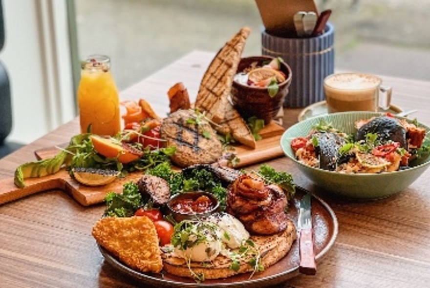 A cooked breakfast plate and a bowl of salad, arranged on a table, with an orange juice and cup of coffee.