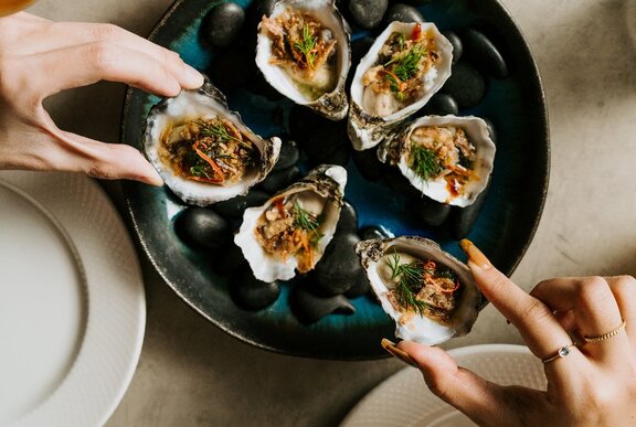 Two people each picking up an oyster from a sharing plate.