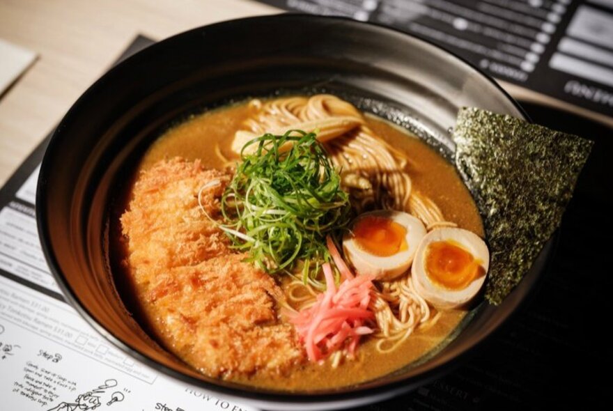 A bowl of Japanese tonkotsu ramen, with crumbed chicken in a curry broth with noodles and two halves of a hard boiled egg.