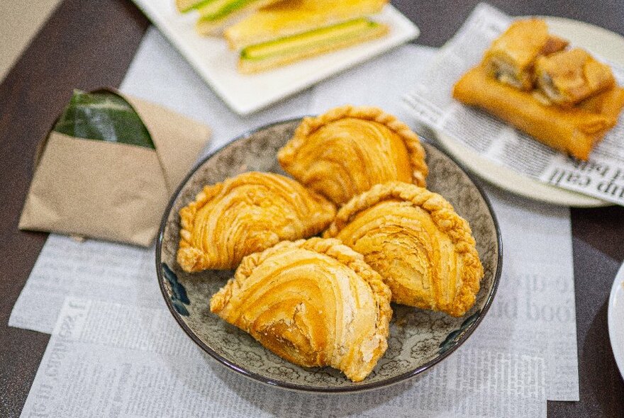 A plate with four curry puffs and other dishes in the background.