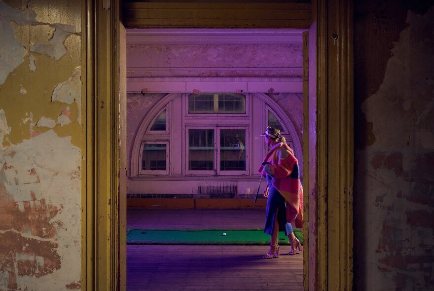 Interior of the upstairs ballroom space at Flinders Street Station, with a green mini-golf putting runner laid out like a long rug, and woman in walking past it.