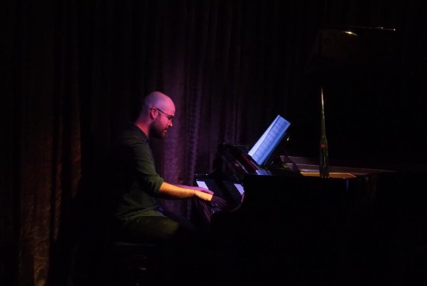 A jazz pianist playing a grand piano on stage in front of a dark purple curtain.