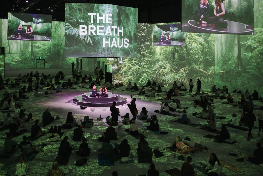 A large green toned area with people gathered for a breathwork class, a projected The Breath Haus sign. 