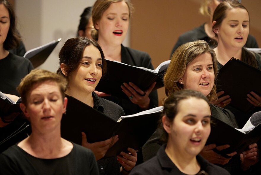 Choir members dressed in black, singing from black songbooks.