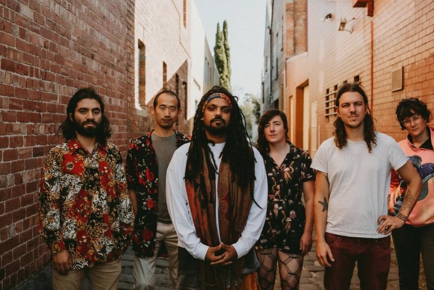 Band members posing in an alleyway looking serious, the lead person has dreadlocks. 