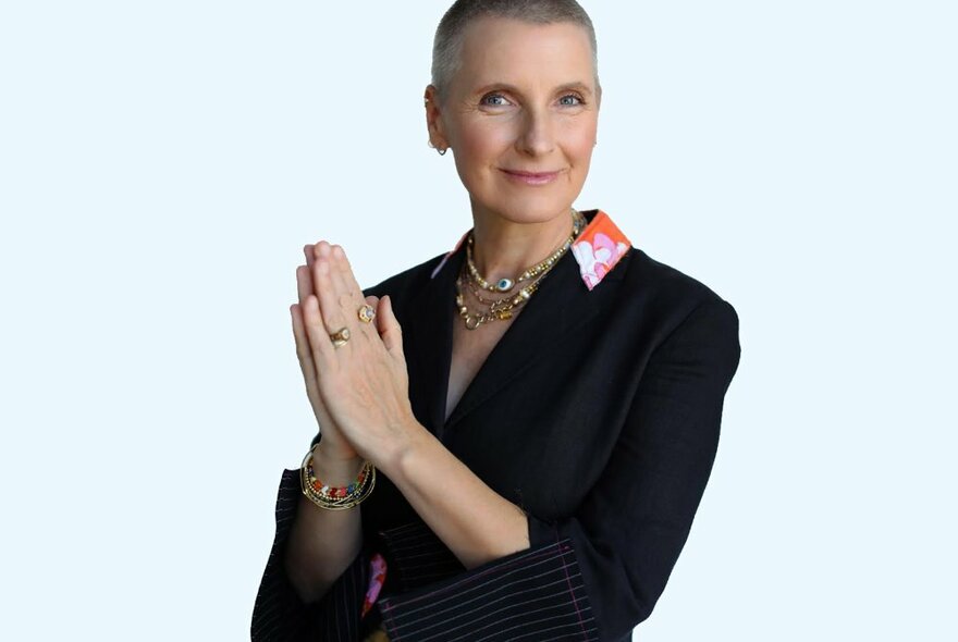 Author Elizabeth Gilbert smiling and holding her hands pressed together in front of her chest, wearing a black shirt that has a patterned collar.