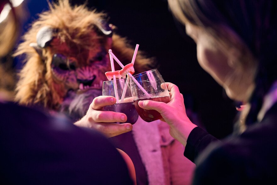 Two people in costumes clinking cocktail glasses together at a party.