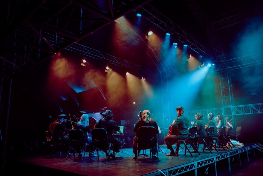 Cellists on a darkened stage with a blue light cast over them. 