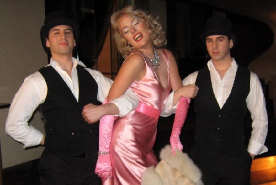 Marilyn Monroe tribute performer wearing pink satin gown, with two men wearing dark waistcoats.