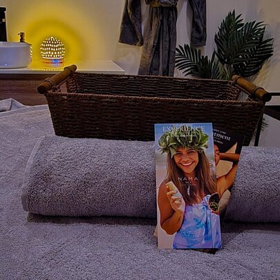 A spa or massage treatment room with a massage bed, rolled grey towel, a brochure and a sink counter in the background.