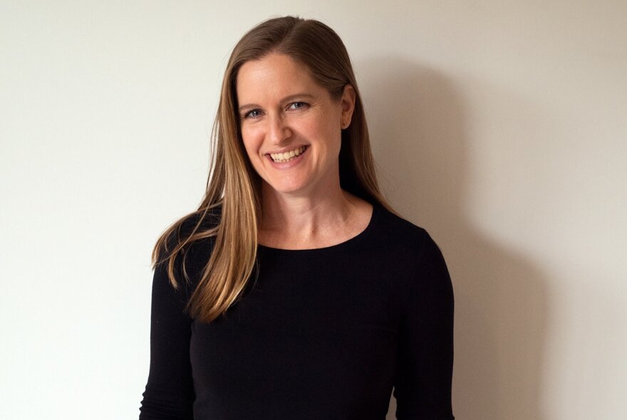 Portrait of a smiling woman with long brown hair, wearing a black top.