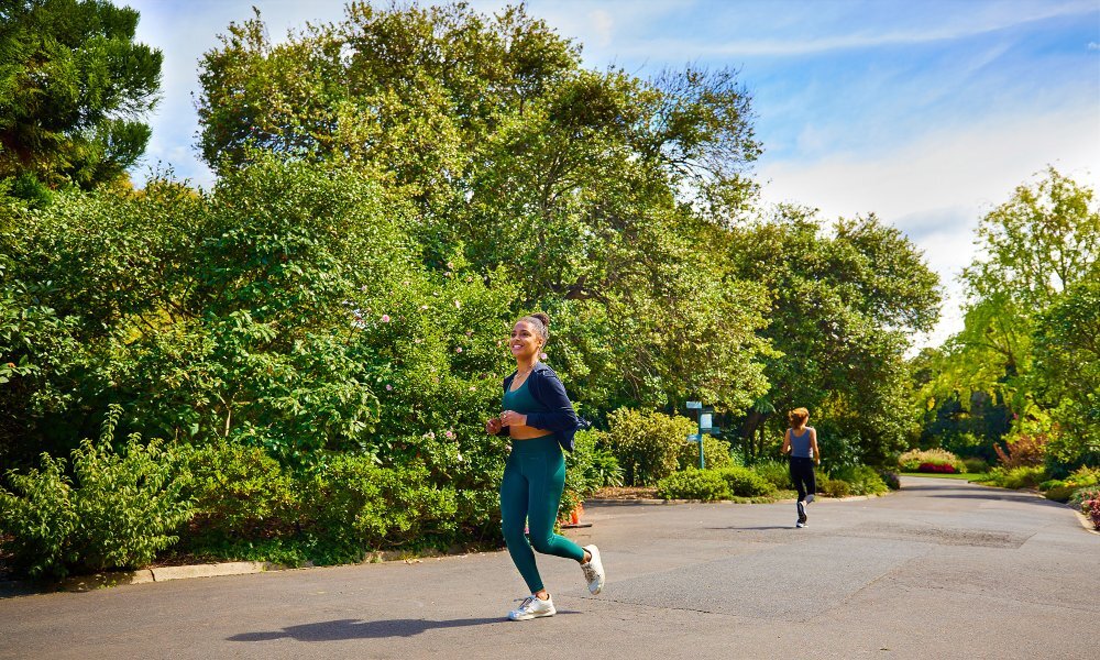 A woman in leggings and a crop top jogging through a garden.