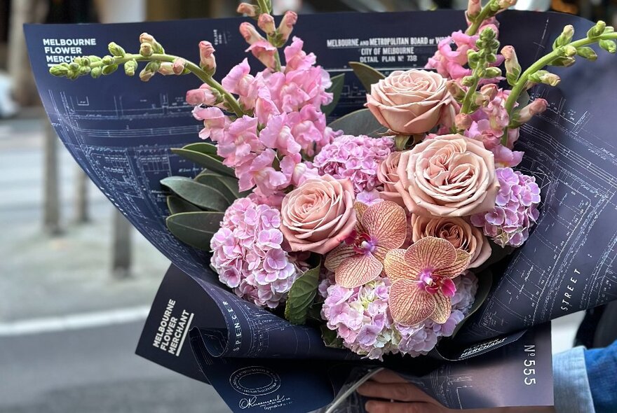 Floral bouquet in shades of pink and green wrapped in distinctive branded dark paper.