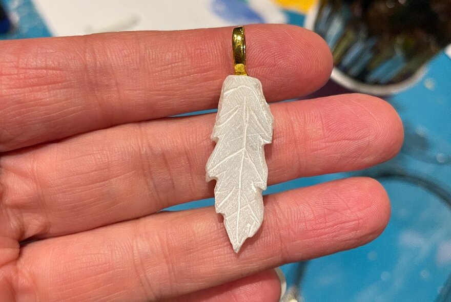 A hand holding a leaf-shaped pendant made from soapstone.