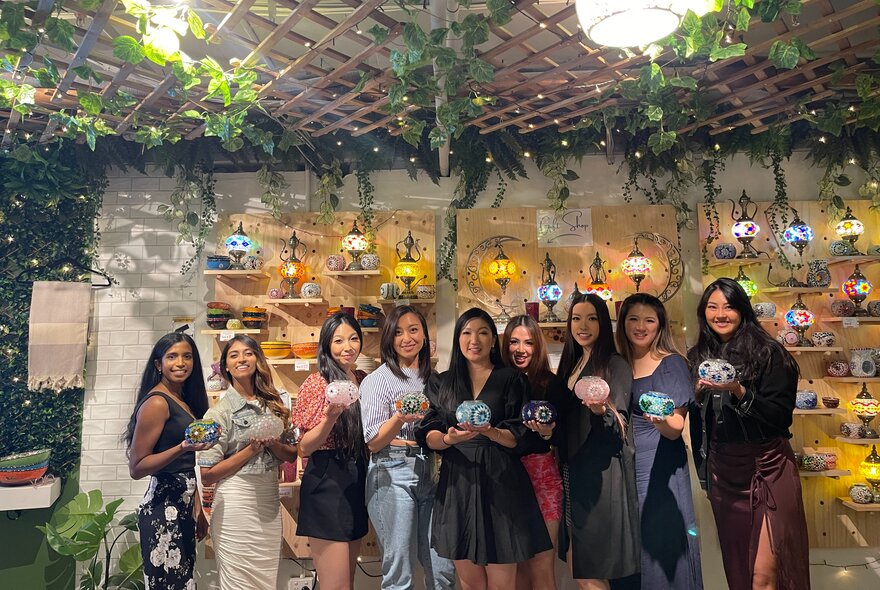 A group of nine women posing for a group shot all holding tiny glass lamps. 