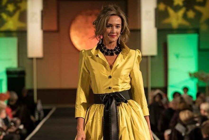 Model on catwalk wearing a belted yellow shirtdress.