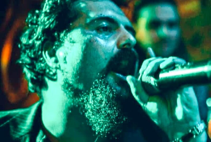 Bearded man singing into a microphone under green lighting.