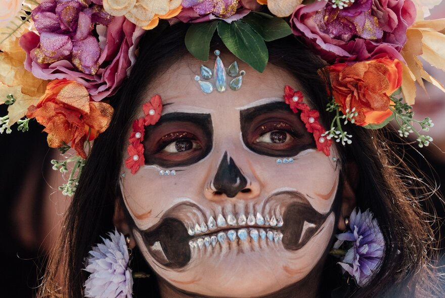 A woman with elaborate Mexican Day of the Dead face paint, making her look like a skeleton, with a floral headdress.