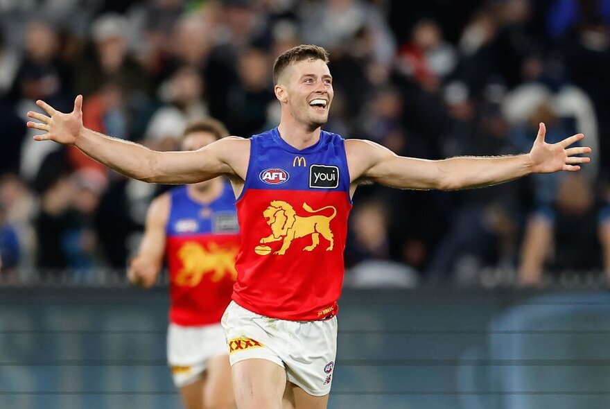 Josh Dunkley from the Brisbane Lions celebrates on the football field, arms outstretched. 