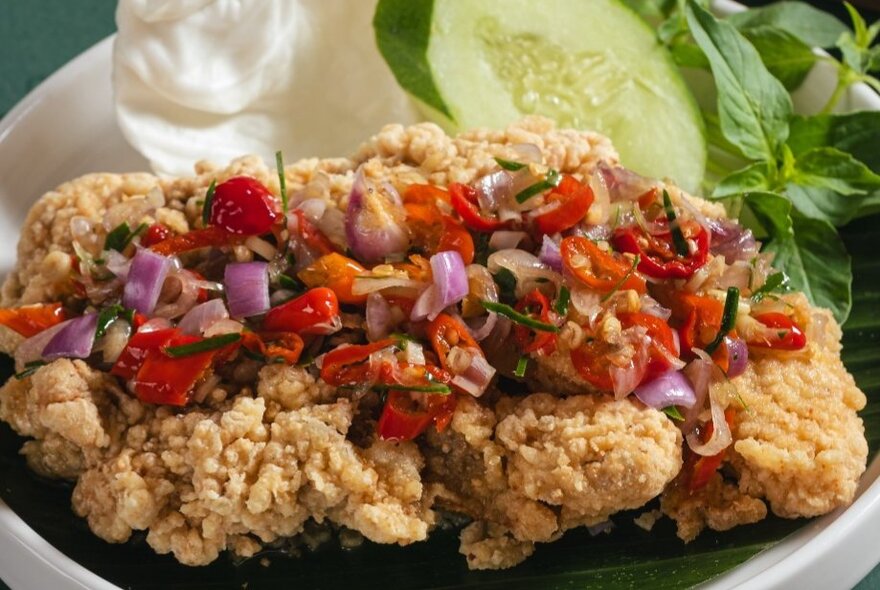 Plate of  ayam geprek, a popular Indonesian dish consisting of crispy battered fried chicken smashed and mixed with a spicy sambal chili condiment. 