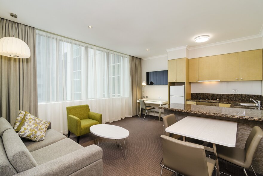 Hotel suite with lounge and dining furniture, kitchen area to one side.