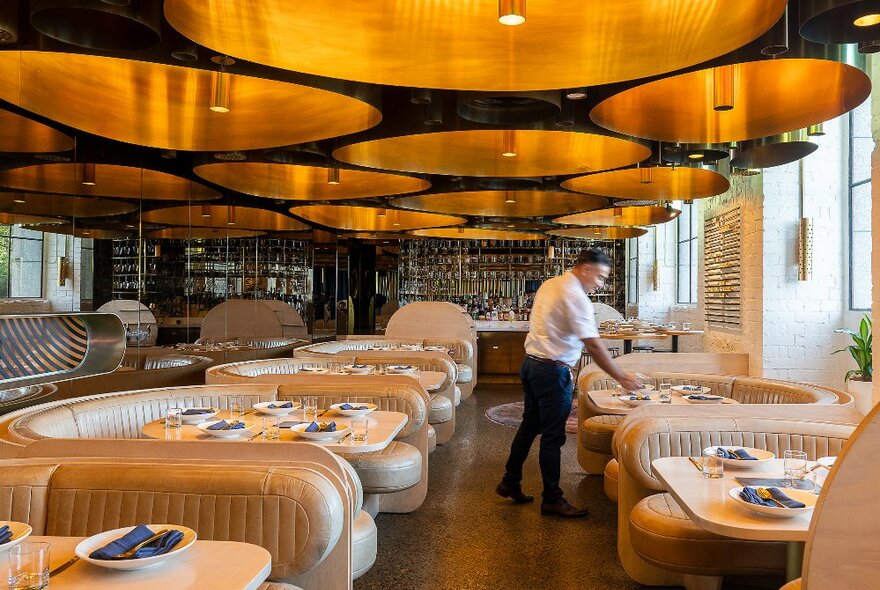 A waiter in a restaurant with large gold ornaments hanging from the ceiling. 