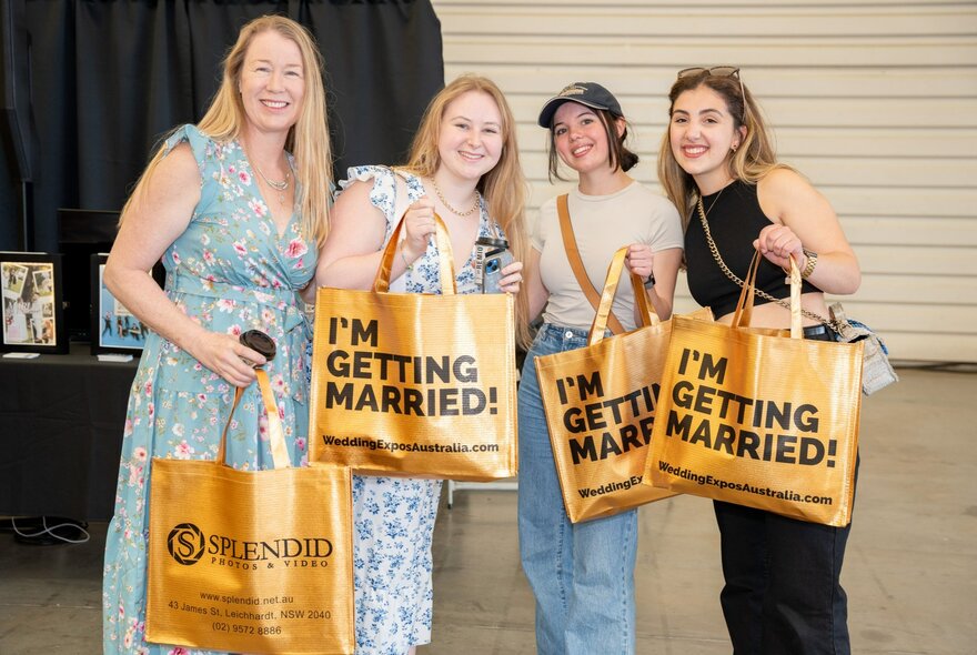 Four women posing while holding up 'I'm getting married' bags.