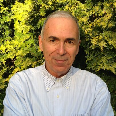 Man wearing a buttoned-up white shirt, standing in front of a yellow-green conifer.