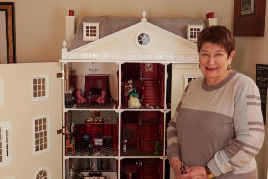 Woman standing next to a Georgian-styled doll's house.