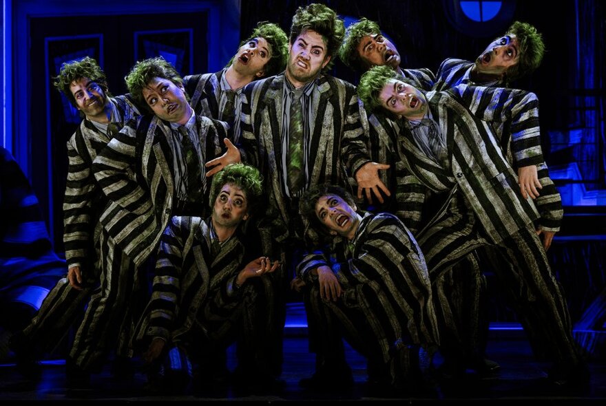 Theatre stage with the cast of Beetlejuice The Musical, all wearing identical striped black and white suits, posed together.